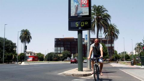 Un joven pasa con su bicicleta junto a un term&oacute;metro que marca 50 grados en una calle de C&oacute;rdoba