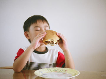 Niño comiendo una hamburguesa, alimento típico en la dieta americana