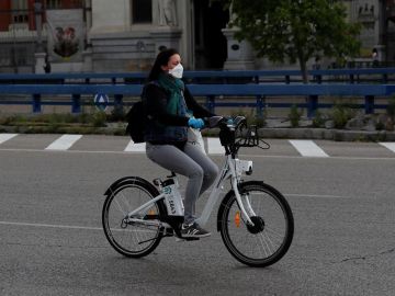 Una mujer con mascarilla y guantes usa una bici de biciMad en Madrid