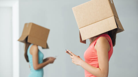 Dos jóvenes, aisladas con cajas de cartón en la cabeza, utilizan su teléfono móvil.