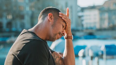 hombre al aire libre se sostiene la cabeza con expresión de dolor hombre al aire libre se sostiene la cabeza con expresión de dolor