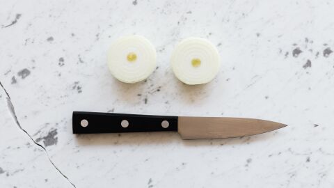Un cuchillo junto a dos trozos de cebolla cortada Un cuchillo junto a dos trozos de cebolla cortada