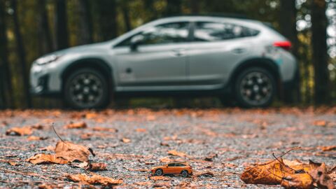 Consejos para poner tu coche a punto para el otoño Plano de fondo con un coche desenfocado, en primer plano un coche en miniatura y suelo de asfalto lleno de hojas de los árboles