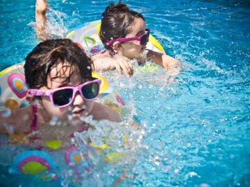 Dos ni&ntilde;as j&oacute;venes disfrutando de un d&iacute;a divertido en una brillante piscina azul con anillos flotantes coloridos.