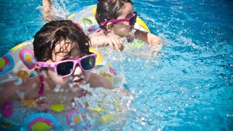 Dos niñas jóvenes disfrutando de un día divertido en una brillante piscina azul con anillos flotantes coloridos. Dos niñas jóvenes disfrutando de un día divertido en una brillante piscina azul con anillos flotantes coloridos.