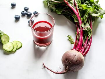 Jugo de remolacha, pepino y ar&aacute;ndano rico en nutrientes con productos frescos sobre fondo blanco