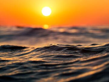 Primer plano de olas del oc&eacute;ano al atardecer con tonos c&aacute;lidos de naranja, capturando la serenidad y la belleza de la naturaleza