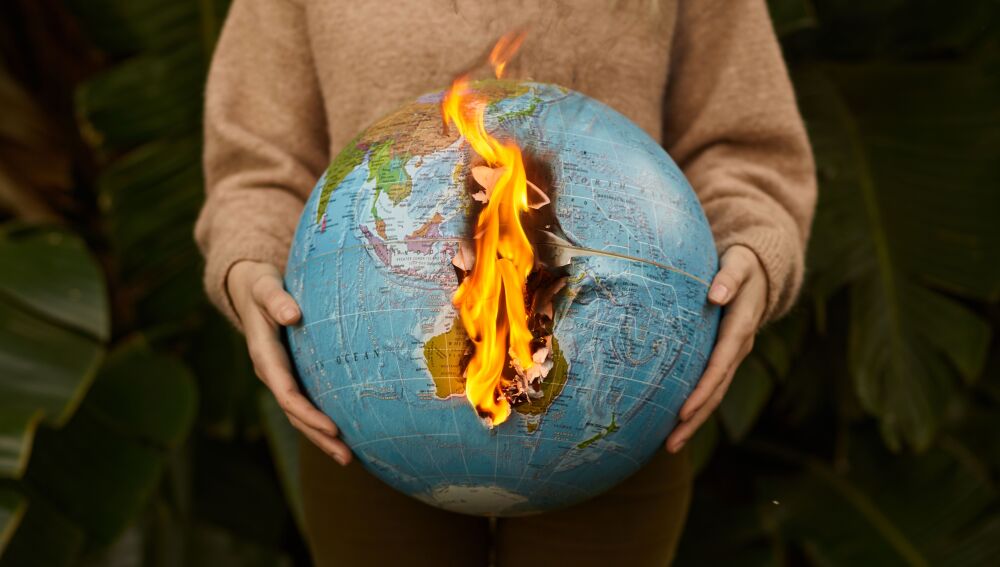 Una representaci&oacute;n simb&oacute;lica del cambio clim&aacute;tico con un globo ardiente sostenido en las manos, en un fondo natural