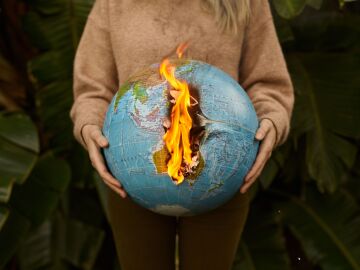 Una representación simbólica del cambio climático con un globo ardiente sostenido en las manos, en un fondo natural Una representación simbólica del cambio climático con un globo ardiente sostenido en las manos, en un fondo natural