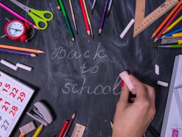 Escribiendo a mano 'vuelta al cole' en una pizarra rodeada de &uacute;tiles escolares