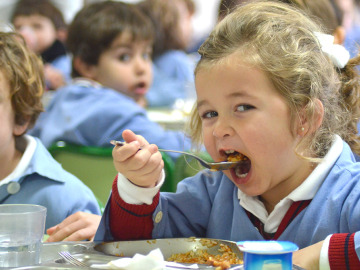 Niña comiendo en un comedor escolar