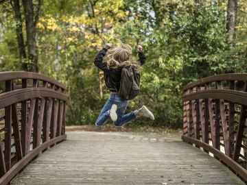 niña con mochila saltando en un puente