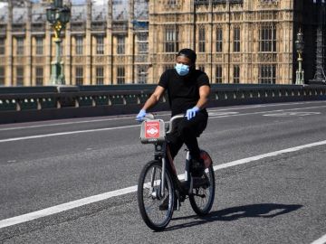 Un hombre con mascarilla circula en bicicleta frente al Parlamento brit&aacute;nico en Londres