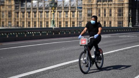 Un hombre con mascarilla circula en bicicleta frente al Parlamento británico en Londres
