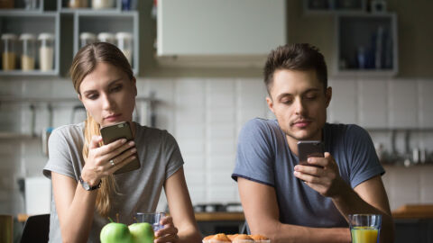 Dos jóvenes desayunando miran atentamente sus móviles. Dos jóvenes desayunando miran atentamente sus móviles.