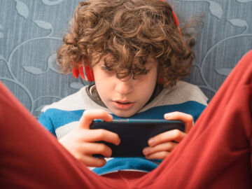 Un adolescente con auriculares y su m&oacute;vil.