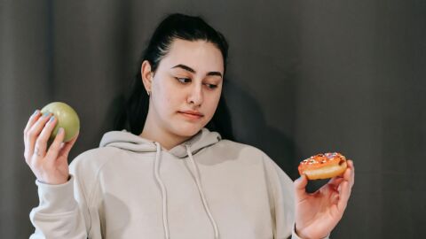 Mujer duda entre alimento sano y un dulce