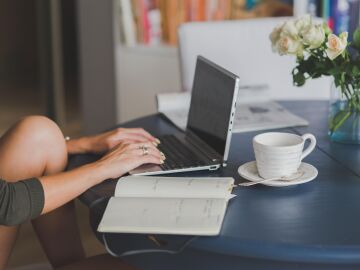 Una persona trabajando en remoto con su ordenador y un café sobre la mesa.