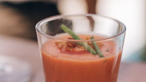 Primer plano de un refrescante gazpacho servido en un vaso transparente con guarnici&oacute;n