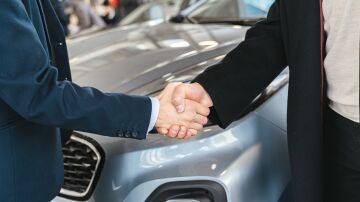 Un primer plano de dos personas estrechando manos frente a un coche en un ambiente interior