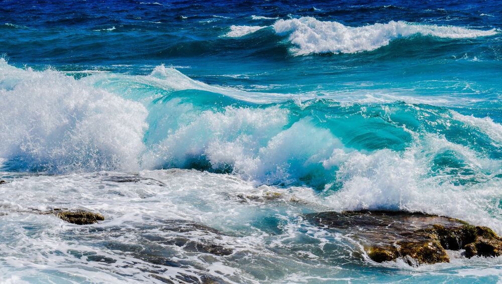 Vibrantes olas azules del océano rompiendo contra la costa rocosa bajo cielos claros de verano. Vibrantes olas azules del océano rompiendo contra la costa rocosa bajo cielos claros de verano.
