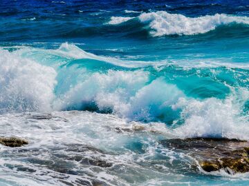 Vibrantes olas azules del océano rompiendo contra la costa rocosa bajo cielos claros de verano. Vibrantes olas azules del océano rompiendo contra la costa rocosa bajo cielos claros de verano.