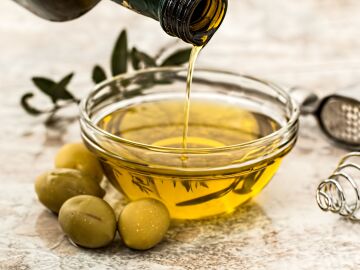 Primer plano de aceite de oliva siendo vertido en un tazón de cristal rodeado de aceitunas frescas y utensilios de cocina. Primer plano de aceite de oliva siendo vertido en un tazón de cristal rodeado de aceitunas frescas y utensilios de cocina.